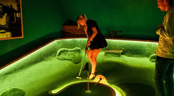 En kvinna spelar minigolf på en bana i Slottskogen. En man tittar på.