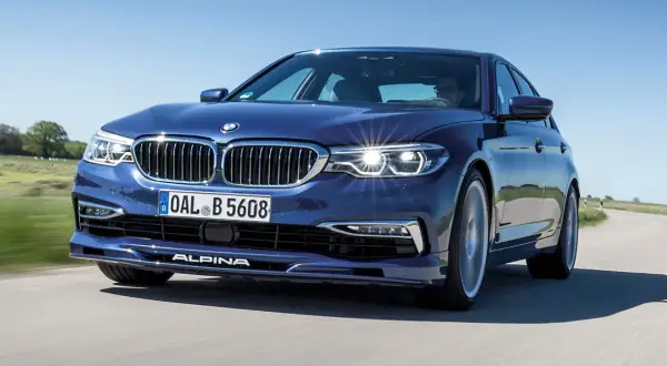 Niebieskie BMW Alpina pędzi po krętej drodze, błyszcząc w słońcu.