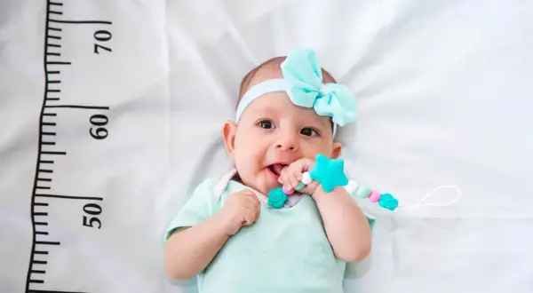 Bebé con diadema azul y mordedor, cerca de una cinta métrica que indica el percentil 15.