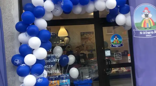 Biało-niebieskie balony tworzą łuk nad wejściem do sklepu z logo Łowicz.
