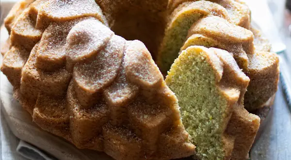 Una deliziosa torta al pistacchio, soffice e profumata, cosparsa di zucchero a velo. La fetta rivela il suo colore verde brillante.