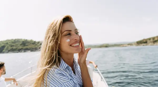 Uśmiechnięta blondynka na łodzi nakłada krem z filtrem, który nie tylko chroni, ale też co przyspiesza opalanie.