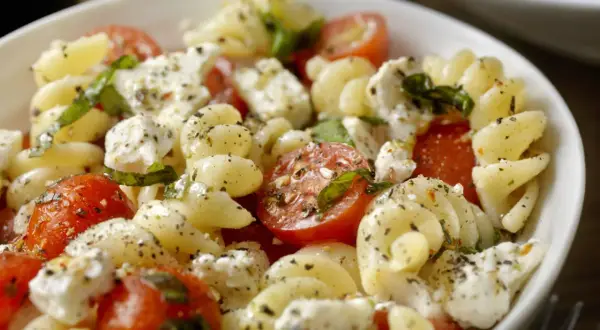 Salade de pâtes froides avec tomates cerises, mozzarella et basilic, assaisonnée d'une vinaigrette légère. Un délice estival.