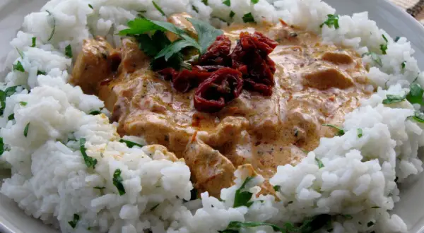 Pyszny kurczak z mascarpone i suszonymi pomidorami, podany z ryżem i posypany natką pietruszki.