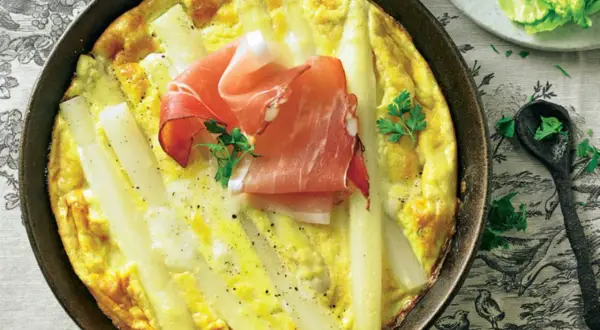 Spargel-Frittata mit Schinken in einer Pfanne, garniert mit Petersilie.