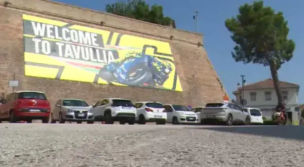 Benvenuti a Tavullia, la terra di Valentino Rossi! Un grande striscione giallo celebra il campione, con auto parcheggiate sotto.