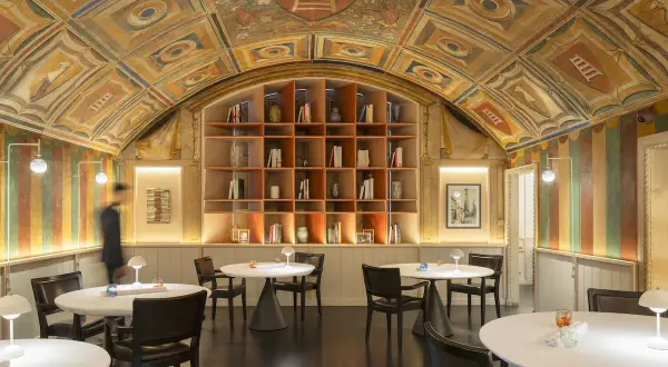Interni eleganti con soffitto affrescato, libreria a vista e tavoli apparecchiati, un'atmosfera che evoca le stelle Michelin di Perbellini.