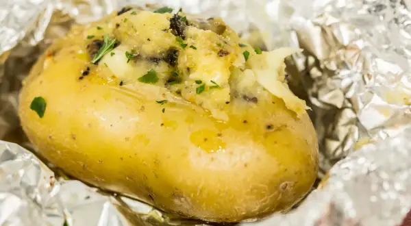 Patate ripiene al forno, dorate e fumanti, avvolte in carta stagnola, con un ripieno cremoso e erbe aromatiche.