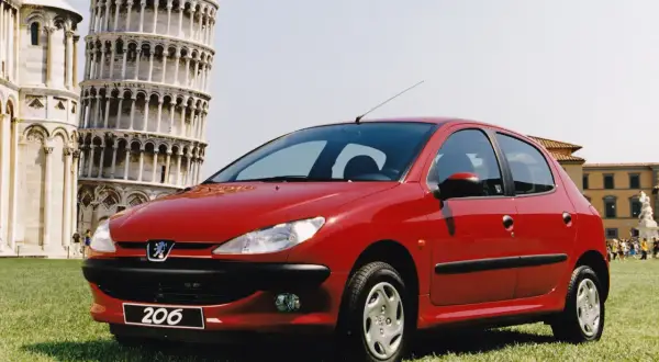 Czerwony Peugeot 206 na tle Krzywej Wieży w Pizie.