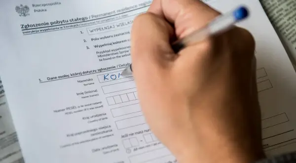 Ręka wypełnia formularz "Zgłoszenie pobytu stałego". Czy jest obowiązek meldunku? Tak, ten dokument to potwierdza.