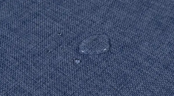 Gocce d'acqua su tessuto blu, dimostrando l'efficacia del lavaggio antimacchia in lavatrice.