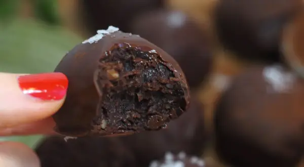 En hand med rött nagellack håller en chokladpralin med dadelfyllning. Perfekt för att baka med dadlar!