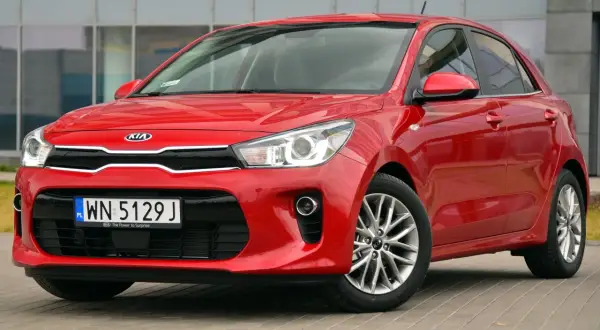 Czerwone Kia Rio przed budynkiem. Wymiana żarówki do jazdy dziennej w tym modelu jest prosta.