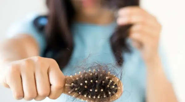 Mujer preocupada por la caída de pelo postparto, mostrando un cepillo lleno de cabello.