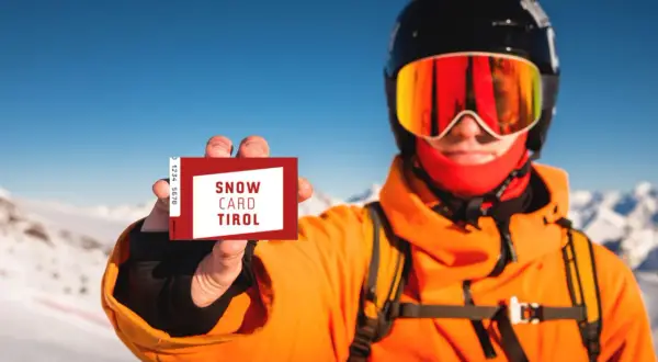 Narciarz w kasku i goglach pokazuje kartę "Snow Card Tirol". To jest skipass, który umożliwia dostęp do wyciągów.