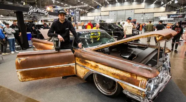 Man bredvid en rostig Oldsmobile 1955 med öppen dörr och motorhuv. Bilen har kromdetaljer och djupa fälgar.