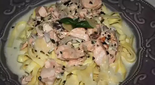 Tagliatelles onctueuses au saumon, parsemées d'herbes fraîches et de poivre noir, servies dans une assiette décorative. Un délice pour les yeux et les papilles.