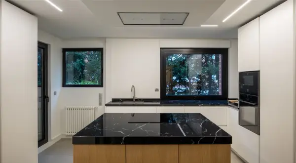 Cocina moderna con **fregadero en isla** de mármol negro y encimeras a juego. Muebles blancos y electrodomésticos integrados.