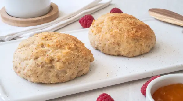 Två gyllene scones på en vit bricka, med hallon och sylt. Perfekt för fika med de godaste scones.