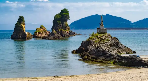 Rocas emergiendo del mar azul, un monumento en una de ellas, y la arena dorada de las playas cerca de Viveiro.