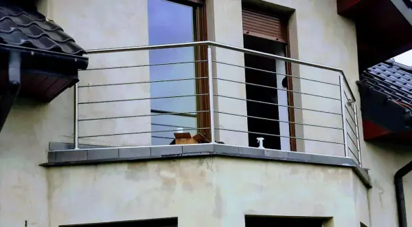 Nowoczesna poręcz ze stali nierdzewnej na balkonie, z widokiem na okna i dachówki.