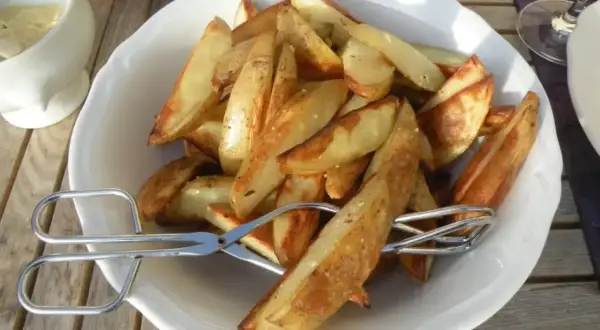 En skål med gyllene klyftpotatis i ugn, redo att serveras med tång.