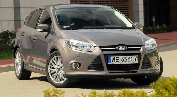 Brązowy Ford Focus MK3, często chwalony w opiniach, prezentuje się elegancko na tle nowoczesnego budynku.