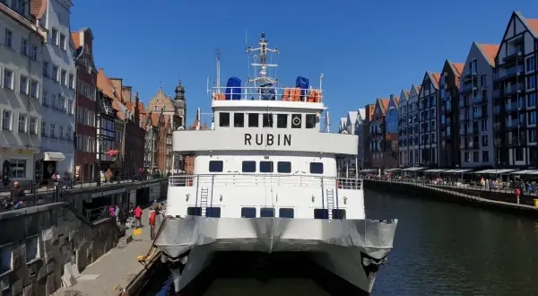 Biały prom "Rubin" cumuje w Gdańsku, gotowy do rejsu na Hel. W tle malownicza starówka i kanał.