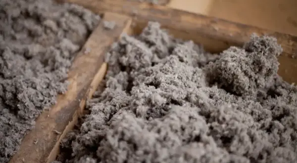 Gros plan sur de la ouate de cellulose grise, un isolant qui peut présenter un danger en cas de mauvaise manipulation.