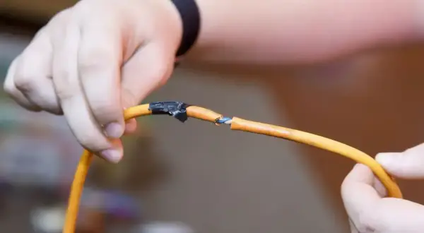 Dłonie łączące pomarańczowy kabel, pokazując jak połączyć kable bez lutowania za pomocą taśmy izolacyjnej.