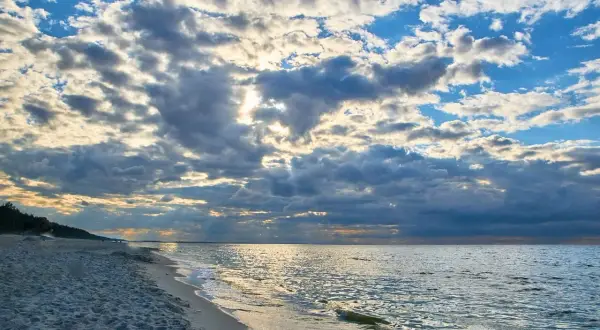 Piękny zachód słońca nad morzem. Chmury na niebie, piaszczysta plaża i spokojne fale. Stegna ile do morza? Niedaleko!