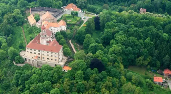 Zamek Nachod w Czechach, otoczony bujną zielenią, z charakterystyczną wieżą i czerwonymi dachami.