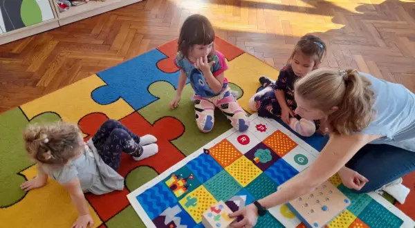 Wspólna zabawa w przedszkolu, gdzie dzieci z autyzmem uczą się przez interakcję. Kolorowa mata i pomoce dydaktyczne wspierają rozwój.