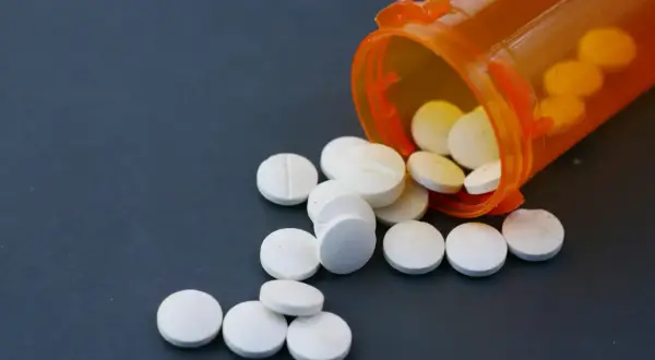 Białe tabletki rozsypane z pomarańczowego pojemnika. Niektóre z nich mogą zawierać fentanyl, substancję o silnym działaniu.