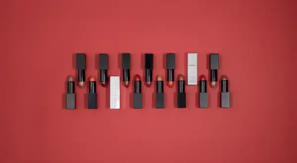 Une collection de rouges à lèvres aux teintes variées, dont un rouge rose éclatant, sur fond rouge.