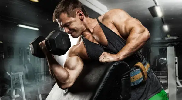 Mężczyzna z determinacją ćwiczy biceps, napinając mięsień trójgłowy ramienia z ciężarem.