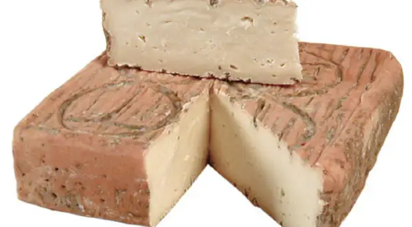 Un pezzo di taleggio bergamasco, con la crosta rosata e la pasta chiara e compatta, tagliato a spicchi.