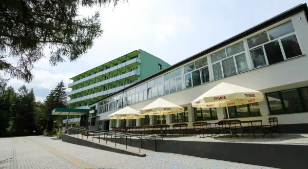 Zielony budynek sanatorium prywatnie, z tarasem i parasolami.