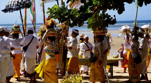 Uczestnicy procesji na plaży, niosący kosze z ofiarami, celebrują balijską religię.