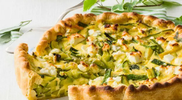 Tarte ricotta courgette dorée, garnie de dés de fromage blanc et de lamelles de courgettes vertes.