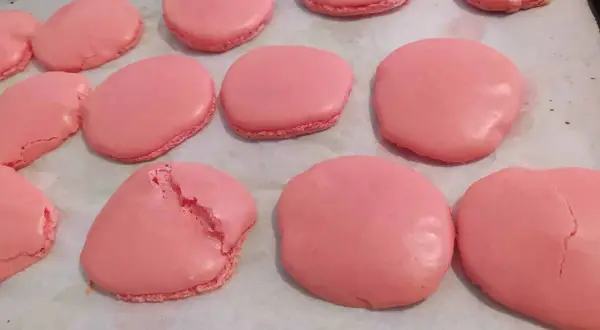 Coques de macarons roses sur une plaque de cuisson. Certaines sont parfaites, d'autres craquent, illustrant pourquoi les macarons craquent.
