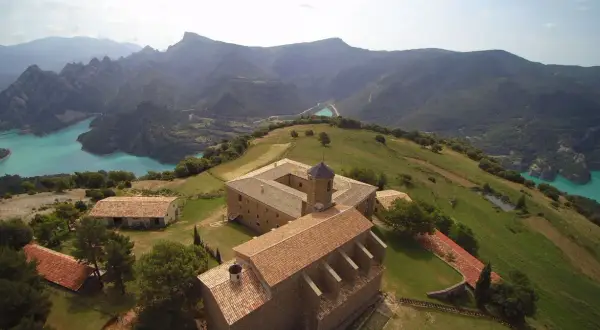 Edificio histórico en la Serra de Busa, con un lago turquesa y montañas al fondo.