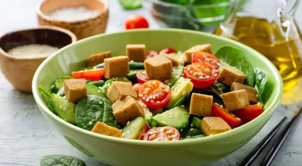 Pyszna sałatka z tofu, pomidorkami koktajlowymi, ogórkiem i szpinakiem, posypana sezamem. Idealna na lekki posiłek.