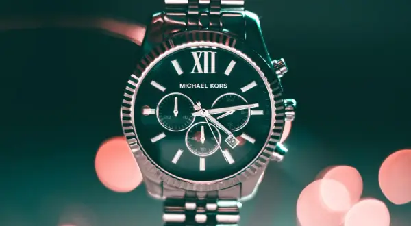Elegancki zegarek Michael Kors z ciemną tarczą i srebrną bransoletą, na tle rozmytych świateł.