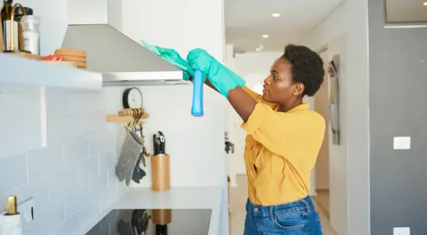 Donna con guanti pulisce la cappa della cucina con uno spray.