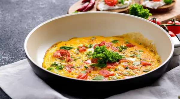 Omlet z pomidorami i ziołami na patelni. Idealny pomysł, jak ograniczyć węglowodany w diecie.