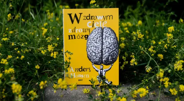 Żółta okładka książki Andersa Hansena "W zdrowym ciele zdrowy mózg" z rysunkiem człowieka dźwigającego mózg, otoczona polnymi kwiatami.