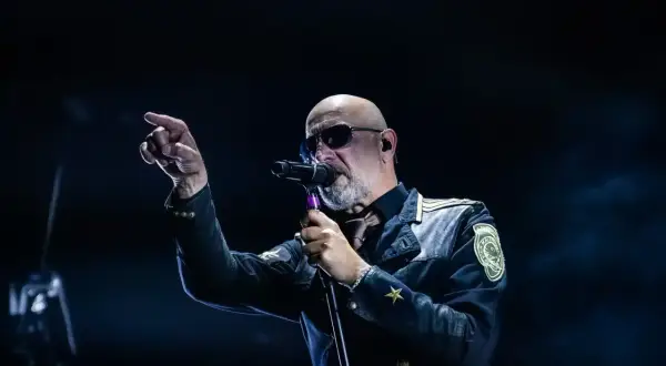 Der Sänger von Eisbrecher Ludwigsburg, mit Sonnenbrille und markanter Jacke, singt ins Mikrofon und zeigt mit dem Finger ins Publikum.