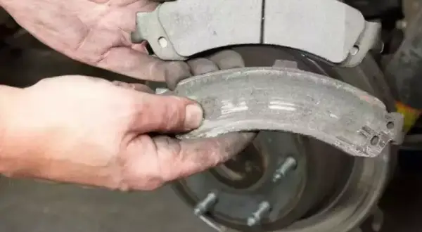 Mani sporche confrontano pastiglie freni nuove e usurate, mostrando il **spessore minimo pastiglie freni** raggiunto da quelle vecchie.