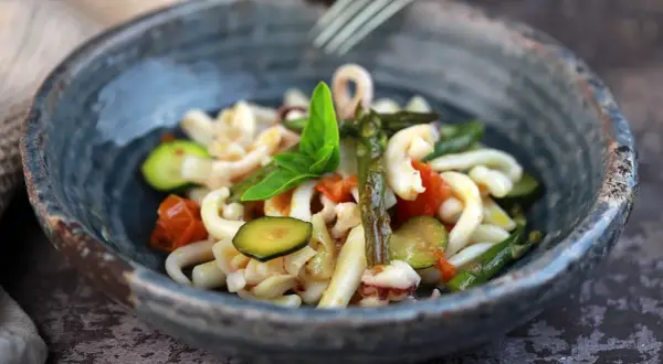 Deliziosa insalata di mare con verdure fresche: calamari, pomodorini, zucchine e asparagi, guarnita con basilico.